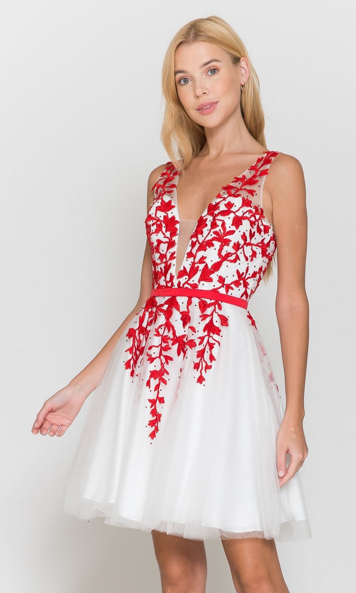 A woman stands against a plain light background wearing the Tulle and Lace Short A-Line Homecoming Dress 8696 in white/red, featuring a sleeveless design with red floral embroidery and a flared skirt.